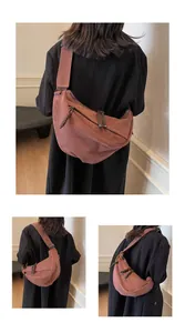 Detail view of the brown crescent canvas bag featuring a woven decorative zipper and wide strap