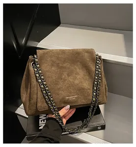 Detail der dunkelbraunen Wildleder-Tragetasche mit Goldlogo und geflochtenem Kettenriemen