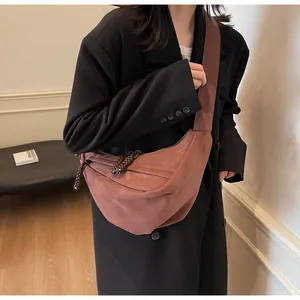 Detail of red-brown suede half-moon crossbody bag with woven knot zipper and wide strap