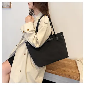 Detailed shot of a large black canvas tote bag with leather straps on a model in a beige coat
