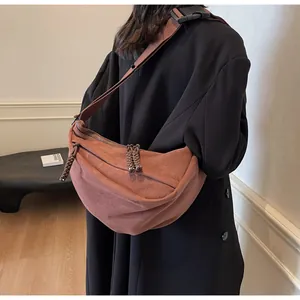 Detail of tan suede crescent bag featuring woven zipper pulls and wide shoulder strap