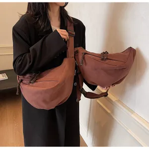 Detail of dark brown crescent crossbody bag with wide strap and woven zipper pull on model