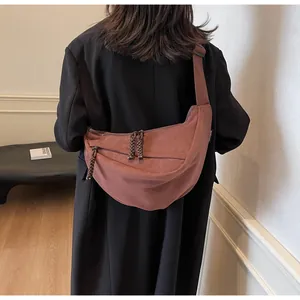 Detail view of brick red half-moon crossbody bag featuring braided rope zipper pulls on a model