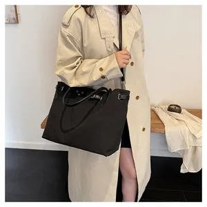 Detail of black canvas tote bag showing faux leather straps and decorative buckle closure