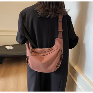 Sac bandoulière en toile rouge brique avec détail de corde tressée porté par un mannequin
