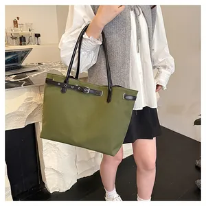 Olive green canvas tote bag with dark leather strap detail worn by model in a stylish cafe