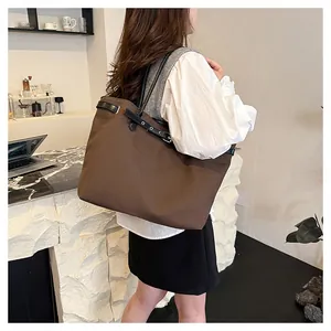 Close-up of minimalist brown tote bag with black leather trim and silver metal eyelets