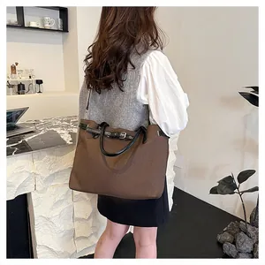 Brown canvas tote bag with black leather handles shown on model in a cafe setting