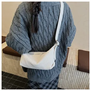 Detail of white pleated crescent bag texture with a long strap on a cable knit sweater