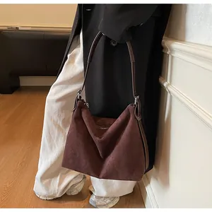 Détail d'un sac cabas en cuir givré bordeaux avec bandoulière marron sur manteau noir