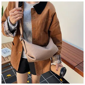 Detail view of the pleat design on the beige crossbody bag worn over a brown corduroy jacket