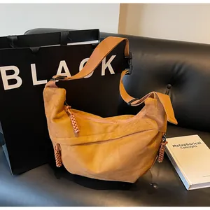 Détail du sac bandoulière en daim jaune moutarde avec nœud tissé sur canapé en cuir noir