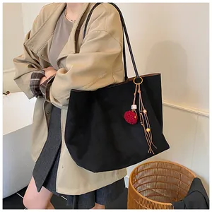 Detailed view of a black large-capacity canvas tote bag with red pompom and wooden bead tassel