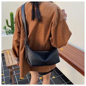 Detail of a black pleated crossbody bag styled with a brown corduroy shirt in autumn