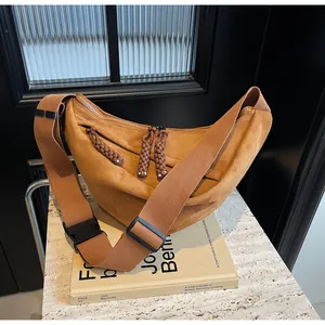 Detail of camel suede crescent bag with woven zipper pullers and wide nylon strap