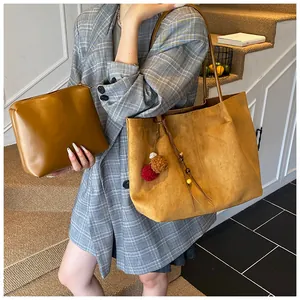 Detail of a ginger yellow suede tote bag and zipper pouch set with tassels on a model