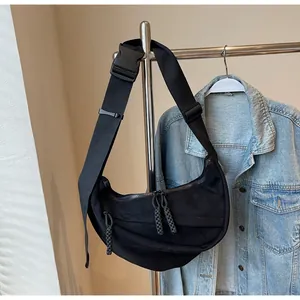 Detail of black crescent crossbody bag with woven rope zipper pulls and buckle strap
