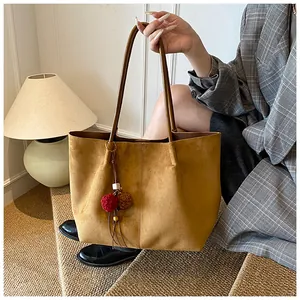 Close-up of brown suede tote bag with decorative pompom keychain and slim leather handles