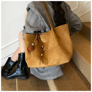 Detail of a large brown suede tote bag featuring ethnic tassels and wooden bead ornaments