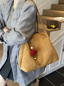 Large mustard suede tote bag with decorative fur pompon charm shown on a model in a gray blazer