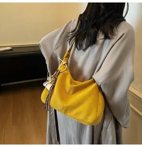 Detail van gele suède hobo-tas met decoratieve franjes en koffie-bedeltje aan tas
