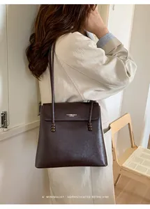 Detail of dark brown leather bucket bag with gold logo and long strap on a wooden chair