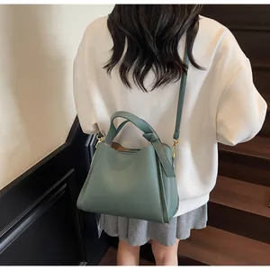 Detail of dark green lychee textured bucket bag with gold hardware on wooden stairs