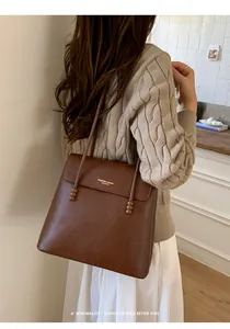 Close-up of vintage brown leather tote bag with elegant beaded pendant and gold lettering