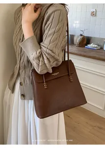 Detail of brown lychee grain leather tote bag featuring gold lettering and bead accents