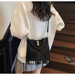 Détail d'un sac seau noir en daim à franges avec fermoir doré porté à l'épaule