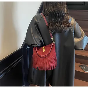 Détail d'un sac seau en daim bordeaux avec de longues franges et un fermoir doré métallique