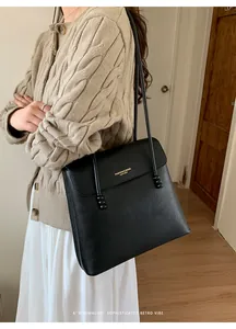 Detail of classic black lychee-grain leather tote bag styled with a beige knit sweater