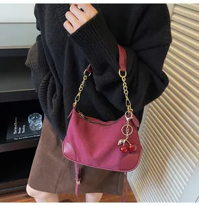 Detail van bordeauxrode suède hobo tas met gouden ketting en kersenhanger bij een model