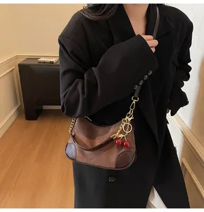 Detail van suède hobo tas met gouden ketting en een rode kersenhanger decoratie