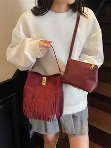 Sac seau en daim bordeaux à franges avec pochette assortie porté avec détails dorés