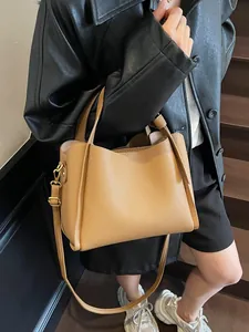 Minimalist tan leather bucket bag with top handles and adjustable shoulder strap