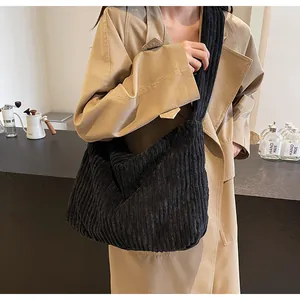 Detail of black corduroy tote bag showing vertical rib texture on shoulder of a trench coat