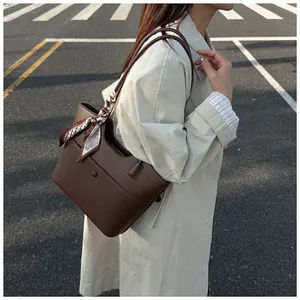 Detail of dark brown leather tote bag with silk scarf and circular buckle accent