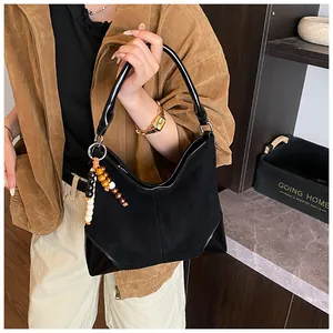 Detalle del bolso tote de ante negro con asas de charol y borla de cuentas de madera
