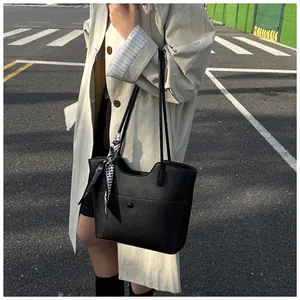 Close-up of black lychee leather tote bag with silk scarf on handle and street fashion detail