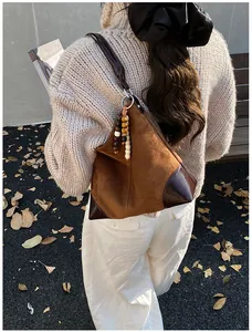 Detalle del bolso tote de ante marrón con colgante étnico y esquinas de piel reforzada