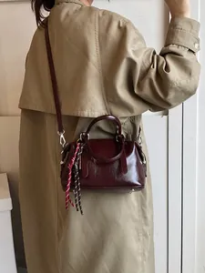 Dames bordeauxrode kunstlederen baguette tas met handvatten gedragen door model in trenchcoat