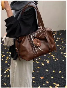 Detail of dark brown faux leather travel bag with plush donut charm and woven strap