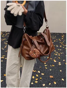 Detail of vintage brown leather tote bag featuring a cute donut charm in autumn setting