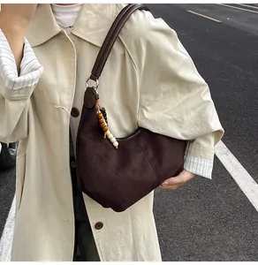 Detail van donkerbruine hobo-tas met suède textuur en kralenhanger op een beige jas