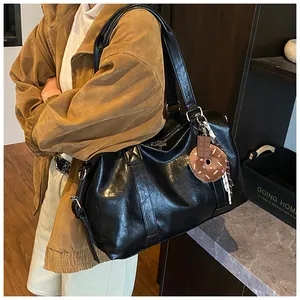 Detail of a large black leather travel tote with zipper and cute charm on a model