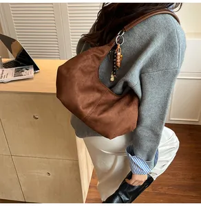 Detail van een bruine suède hobo-tas met etnische kralenhangers en ronde lederen riem