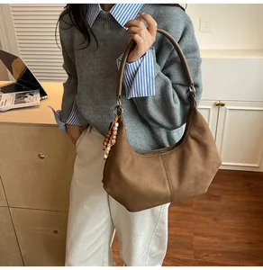 Detail van een grote bruine suède hobo tas met kralenhanger en stikseldecoratie