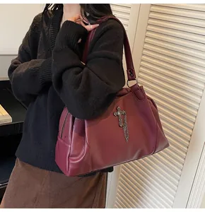 Detail view of burgundy leather tote with a metal cross charm for casual fashion wear