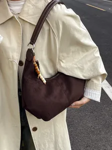 Donkerbruine suède schoudertas met houten kralen gedragen op een beige trenchcoat